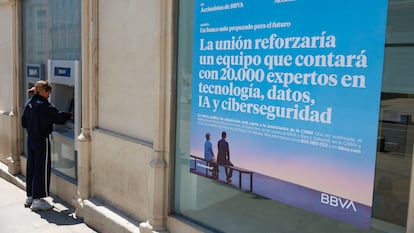Una mujer saca dinero de un cajero del BBVA en Madrid este martes junto a la publicidad del banco sobre la opa al Banco Sabadell.