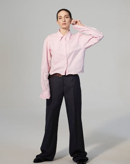 En esta fotografía, la actriz lleva camisa rosa, pantalones grises con detalle de dibujo de cinturón y mocasines de charol negro, todo de Prada.
