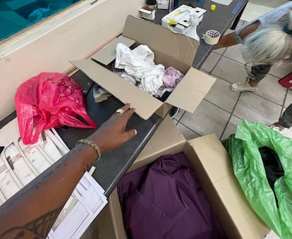 A woman shows one of the boxes of used clothing that she inherited from a deceased person, in a license plate and billboard store in the Roodepoort industrial area in Johannesburg, South Africa. A pair of beige pants that EL PAÍS tracked is presumably in one of the boxes.